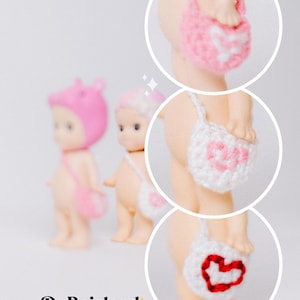 以下が含まれることがあります： ピンク、白、赤のハート型の編み物アクセサリーを身につけた、3体の小さなヌードカラーの人形。DuBoislandのロゴが画像の下部に表示されています。