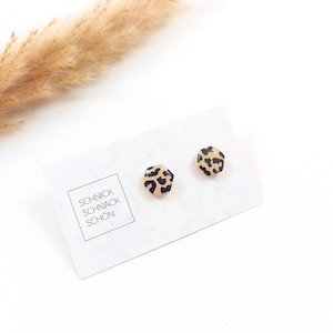 Peut inclure: Une paire de petites boucles d'oreilles hexagonales à clous avec un motif léopard. Les boucles d'oreilles sont sur une carte blanche avec le texte "Schnick Schnack Schön".