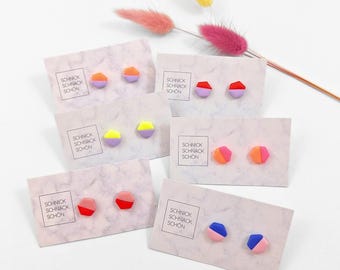 Puede incluir: Seis pares de pequeños pendientes de botón hexagonales presentados en tarjetas individuales con patrón de mármol. Cada pendiente tiene un diseño bicolor en tonos vibrantes como naranja, morado, rojo, amarillo, rosa y azul. Cada tarjeta tiene impreso el texto SCHNICK SCHNACK SCHÖN.
