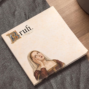 May include: A square notepad with the word "Bruh" in a decorative font. The notepad features an illustration of a woman in Renaissance attire, looking upwards with a thoughtful expression. The notepad is on a wooden desk.