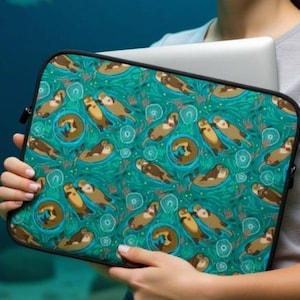 May include: Teal laptop sleeve featuring a repeating pattern of otters, with a black border. The otters are brown and tan, set against a teal background with white swirls and circular designs. The sleeve is held by a person in front of an underwater background.