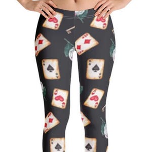May include: Dark grey leggings patterned with playing cards, keys, and floral motifs. The cards display red hearts and diamonds, and black spades and clubs. These leggings are a comfortable and fashionable item of clothing.