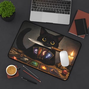 Puede incluir: Alfombrilla de ratón con un gato negro sosteniendo un cuchillo y cartas del tarot. El diseño incluye una vela encendida, dados y una taza de café. La alfombrilla está sobre una superficie oscura.
