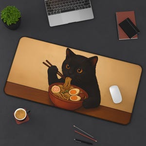 Puede incluir: Alfombrilla de escritorio rectangular con un gato negro comiendo ramen. El gato tiene ojos naranjas y sostiene palillos. El cuenco de ramen es rojo y el fondo es beige con un borde marrón. Un ratón blanco está a la derecha.