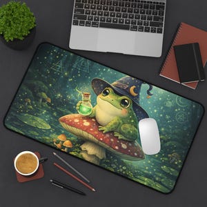 May include: A whimsical mousepad featuring a cartoon frog wearing a witch hat and sitting on a mushroom. The frog holds a potion bottle. The background depicts a magical forest scene with glowing lights and mushrooms.