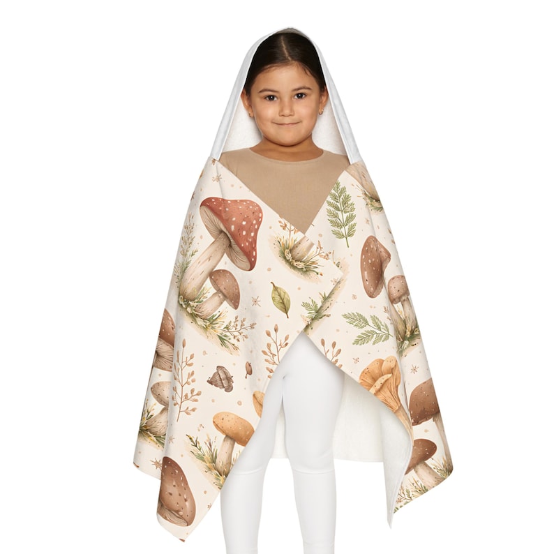 Peut inclure: Une serviette &agrave; capuche avec un motif de champignons marron, beige et vert. La serviette a une capuche blanche et un design enveloppant. Le motif pr&eacute;sente des illustrations de diff&eacute;rents champignons et feuilles. Parfait pour s&eacute;cher apr&egrave;s le bain ou la baignade.
