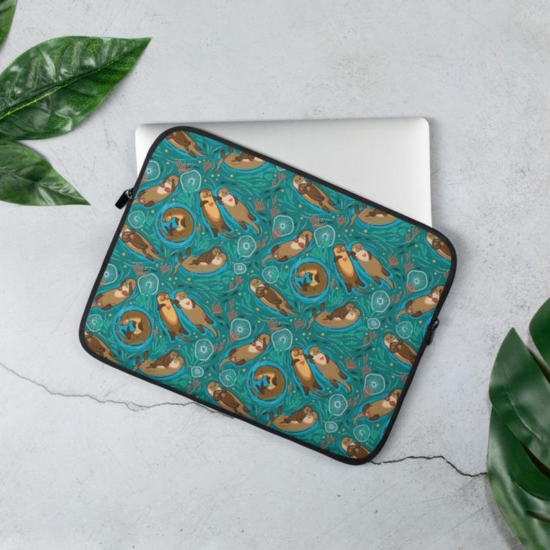 May include: A teal laptop sleeve featuring a repeating pattern of cartoon otters in various poses. The otters are brown and tan, set against a background of teal water and green foliage. The sleeve has a black zipper and trim.