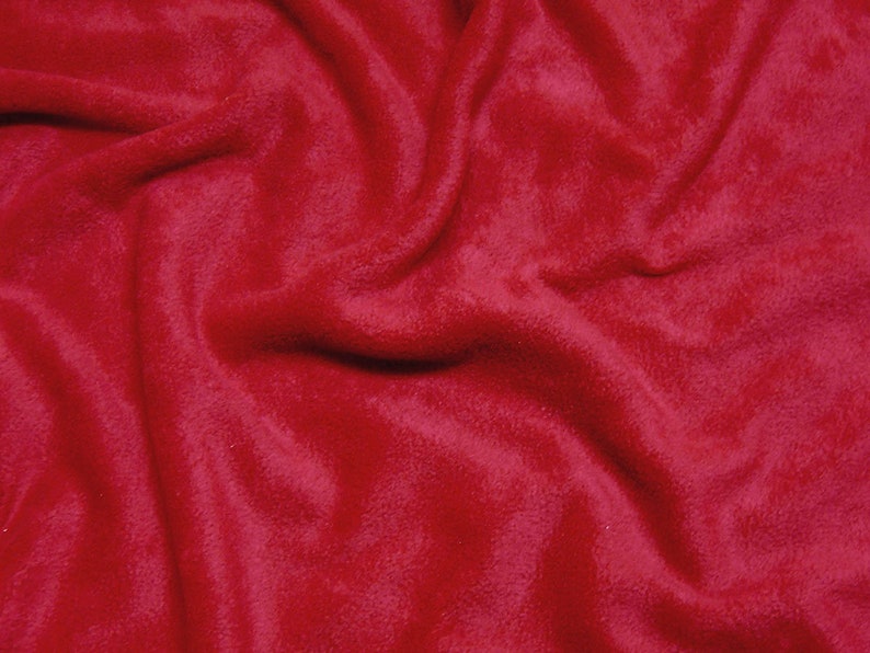 May include: A close-up of a soft, red fleece fabric. The fabric is wrinkled and has a fuzzy texture.