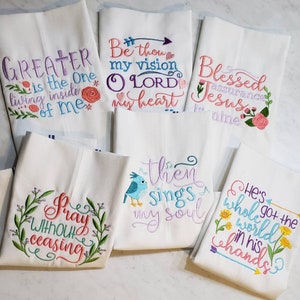 May include: Six white kitchen towels with embroidered inspirational quotes and floral designs. The quotes include "Greater is the One living inside of me", "Be thou my vision O LORD my heart", "Blessed assurance Jesus is mine", "Pray without ceasing", "Then sings my soul", and "He's who got the whole world in his hands".