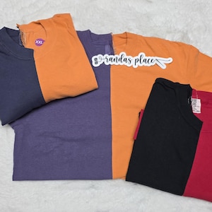 May include: A collection of long-sleeved t-shirts in various colors, including navy blue, orange, purple, black, and red. Some shirts have tags and labels. The text "randas place" is visible on one shirt.