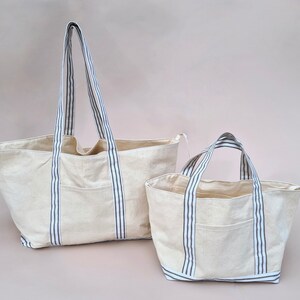 Peut inclure: Deux sacs cabas en toile avec des anses ray&eacute;es bleu et blanc. Le plus grand sac a une seule poche sur le devant. Le plus petit sac a une seule poche sur le devant.