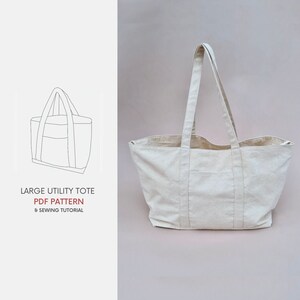 Puede incluir: Una bolsa de lona beige grande con dos asas anchas. La bolsa tiene un bolsillo grande en la parte delantera y se muestra sobre un fondo beige claro. El texto "LARGE UTILITY TOTE PDF PATTERN 6 SEWING TUTORIAL" est&aacute; impreso debajo de la bolsa.