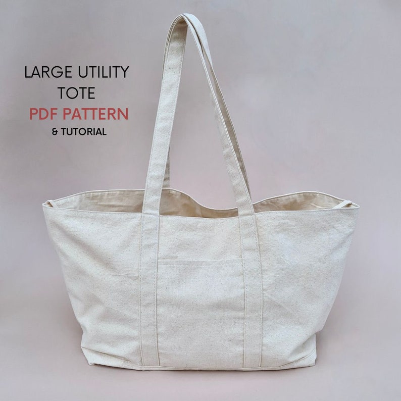 Puede incluir: Una bolsa de lona grande de color blanco roto con dos asas largas. La bolsa tiene una forma rectangular con un fondo ligeramente redondeado. El texto "LARGE UTILITY TOTE PDF PATTERN & TUTORIAL" est&aacute; impreso en la esquina superior izquierda de la bolsa.