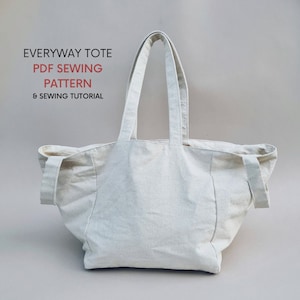 May include: A white canvas tote bag with long handles. The bag is empty and has a simple design. The text "EVERYWAY TOTE PDF SEWING PATTERN & SEWING TUTORIAL" is printed on the top of the image.