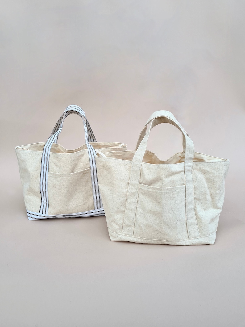 Peut inclure: Deux sacs cabas en toile beige avec des anses ray&eacute;es. Un sac a une seule poche sur le devant, tandis que l'autre a deux poches.