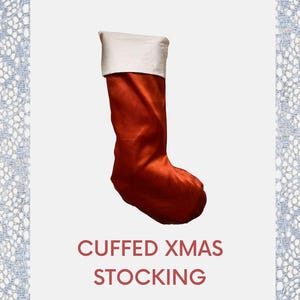 May include: A Christmas stocking with a burnt orange body and a white cuff. The text "CUFFED XMAS STOCKING" is displayed in red. The stocking is set against a white background with a decorative lace border.