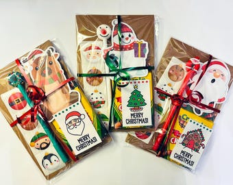 May include: Three gift bags filled with Christmas-themed items, including stickers, a pen, and a card that says "Merry Christmas!" Each bag is tied with a red ribbon and decorated with festive paper.