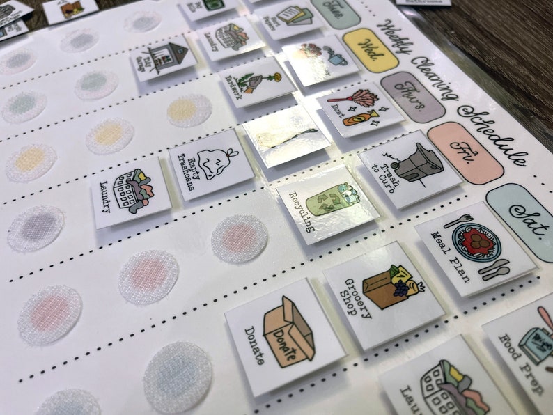 May include: A white weekly cleaning schedule chart with colourful squares and icons for each day of the week. The icons include a broom, a bin, a recycling bin, a shopping bag, a laundry basket, and more. The chart is designed to help people stay organised and on top of their cleaning tasks.