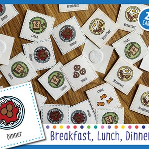 May include: A set of 24 cards featuring illustrations of different foods, categorized as breakfast, lunch, and dinner. The cards are printed on white cardstock with colorful borders and feature images of foods like eggs, toast, spaghetti, and pretzels.