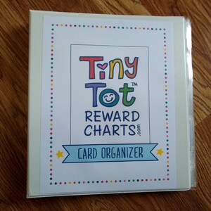 May include: White binder with a colorful border and the text "Tiny Tot&trade; Reward Charts.com Card Organizer" in the center.