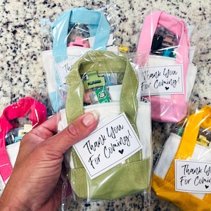 May include: Small canvas tote bags in light blue, pink, olive green, hot pink, and yellow, each individually wrapped in clear plastic. Each bag features a white tag with the black printed text Thank You For Coming! and a small heart icon.