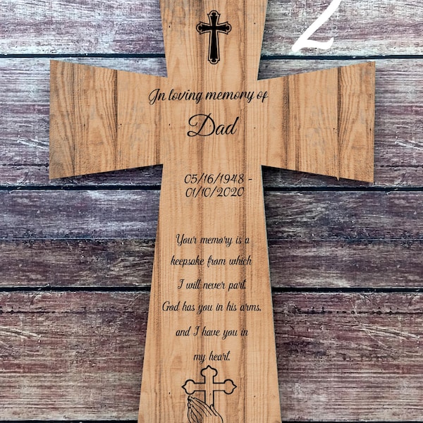 May include: A wooden cross with a white string hanging from the top. The cross is engraved with the words "In loving memory of Dad", the dates "05/16/1948 - 01/10/2020", and a poem about remembering a loved one. The cross is on a wooden background.