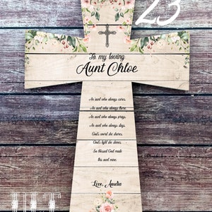 May include: A wooden cross with a floral design and the text "To my loving Aunt Chloe" and "Love, Amelia". The cross is decorated with pink and white flowers and green leaves. The number 23 is written in white on the top right corner of the cross.