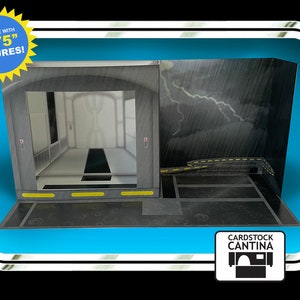 May include: A gray and black cardboard model of a Star Wars cantina interior, designed for use with 3.75 inch action figures. The model features a doorway leading to a hallway, a stormtrooper-themed hallway, and a rainy exterior with lightning.