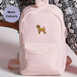 Peut inclure: Un sac à dos en toile rose avec une petite image brodée d'un chien brun. Le sac à dos a une poche zippée à l'avant et des bretelles réglables.