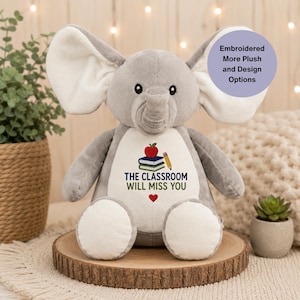 Op de afbeelding: Een grijze pluche olifant met grote oren en een witte buikvlek. De buik is voorzien van een geborduurd ontwerp van een rode appel, een stapel boeken, een geel potlood, een klein rood hartje en de tekst THE CLASSROOM WILL MISS YOU.