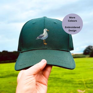 Puede incluir: Una gorra de béisbol verde con un diseño de gaviota bordado. La gorra tiene una visera curvada y una correa ajustable.