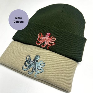 May include: Two knitted beanies with embroidered octopus designs. The top beanie is dark green with a red octopus. The bottom beanie is beige with a blue octopus.