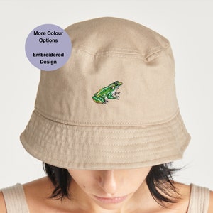 May include: A beige bucket hat with an embroidered green frog design. More colour options are available.