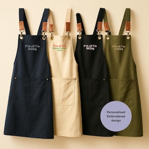 Pode incluir: Quatro aventais em azul-marinho, bege, preto e verde-oliva, cada um com um bolso frontal, detalhes de alças em couro marrom e ferragens metálicas. O texto bordado no peito diz: F*ck off I'm Baking, F*ck off I'm Making Christmas Dinner, F*ck off I'm BBQing e F*ck off I'm Cooking.