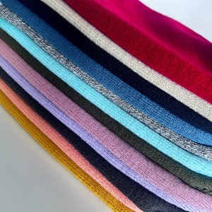 May include: A stack of 14 different coloured knitted fabric swatches. The swatches are arranged in a rainbow pattern, with the top swatch being a bright red and the bottom swatch being a mustard yellow.