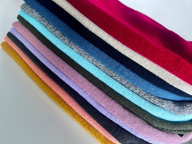 May include: A stack of 14 different coloured knitted fabric swatches. The swatches are arranged in a rainbow pattern, with the top swatch being a bright red and the bottom swatch being a mustard yellow.