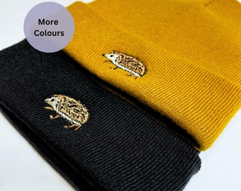 May include: Two knitted beanies, one black and one mustard yellow, both featuring an embroidered hedgehog design.