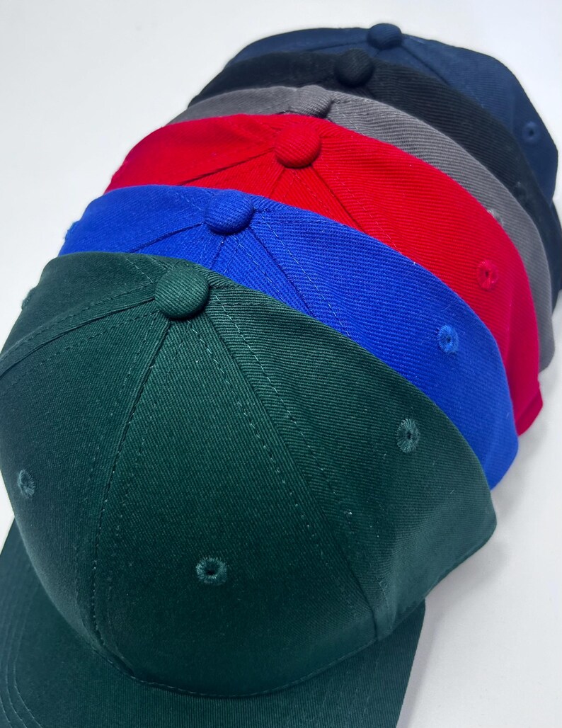 May include: A collection of baseball caps in various colors, including green, blue, red, gray, and navy. Each cap has a curved brim and a button on top. The caps are arranged in a row, showcasing the different color options.