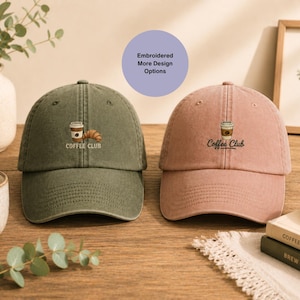 Pode incluir: Duas bonés de beisebol, uma verde-oliva e outra rosa empoeirado, são exibidos. Cada boné apresenta um design bordado de xícara de café e croissant, com as palavras "Coffee Club" abaixo. Um círculo roxo com texto está no fundo.