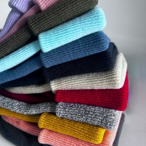 Puede incluir: Una pila de 15 diademas de punto en varios colores, incluyendo morado, rosa, verde, azul, gris, rojo y amarillo. Las diademas est&aacute;n dispuestas en forma de pir&aacute;mide.