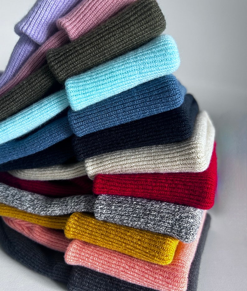 Puede incluir: Una pila de 15 diademas de punto en varios colores, incluyendo morado, rosa, verde, azul, gris, rojo y amarillo. Las diademas est&aacute;n dispuestas en forma de pir&aacute;mide.