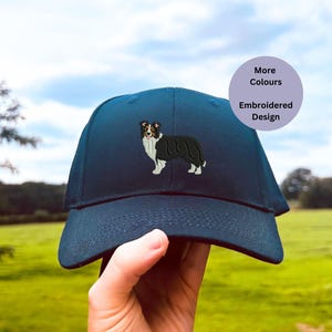 Puede incluir: Una gorra de béisbol azul oscuro con un diseño bordado de un border collie negro y blanco.