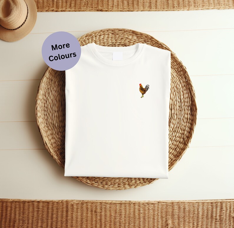 May include: White t-shirt with a small embroidered rooster design. The rooster is brown and yellow with a red comb.