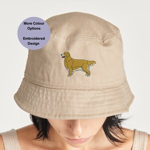 Beige cotton bucket hat worn by model featuring small embroidered golden retriever dog design on front with soft structured brim and neutral background