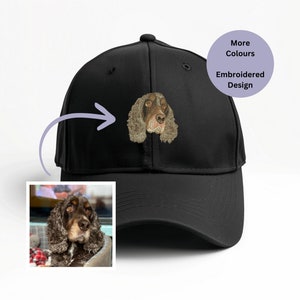 May include: A black baseball cap featuring an embroidered design of a dog's face in shades of brown and tan. The cap has a curved peak and a button on top. The image also includes a small photo of the dog and text that says "More Colours" and "Embroidered Design".