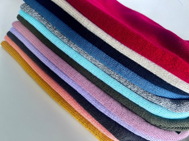 May include: A stack of 14 different colored knitted fabric swatches. The swatches are arranged in a rainbow pattern, with the top swatch being a bright red and the bottom swatch being a mustard yellow.