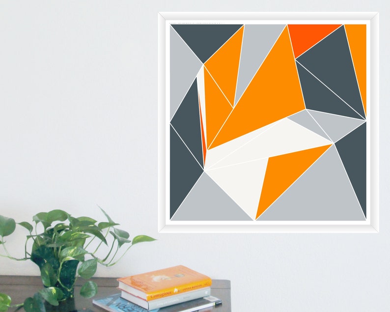May include: Geometric abstract art print in a white frame. The artwork features a design of triangles in shades of orange, grey, and white. The artwork is displayed on a white wall.