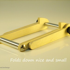 May include: A wooden folding frame with silver metal bars and black knobs. The frame is light-colored wood and folds down for compact storage. Text on the image reads "Folds down nice and small."