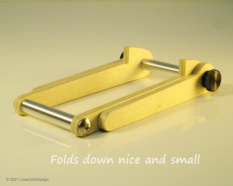 May include: A wooden folding frame with silver metal bars and black knobs. The frame is light-colored wood and folds down for compact storage. Text on the image reads "Folds down nice and small."