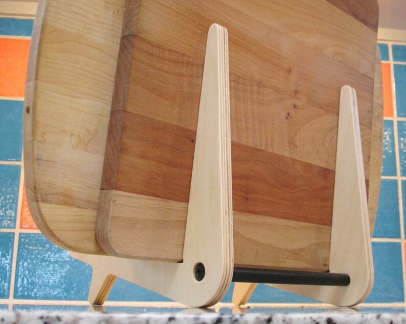 May include: Wooden cutting boards in a light wood tone are displayed in a light wood stand. The stand has a minimalist design with a black bar at the bottom. The cutting boards are various sizes and shapes.